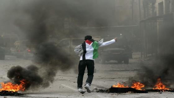 JERUSALEM - MARCH 19: A Palestinian youth wearing a Palestinian flag throws rocks at Israeli border police, during violent clashes in Shuafat refugee camp, on March 19, 2010, in Jerusalem, Israel. Hundreds of Palestinian youth clashed with Israeli police throughout East Jerusalem, in response to further closures of a the Al-Aqsa mosque inside the Old City to men under 50 and growing tensions over Israel's plans to build more houses in East Jerusalem. (Photo by Warrick Page/Getty Images)
